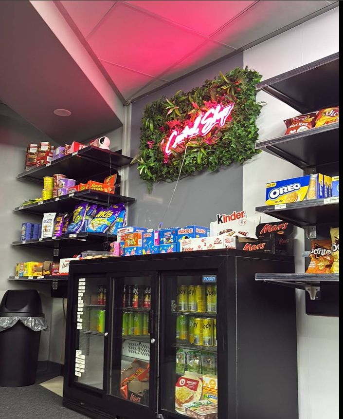 L'intérieur du Central Shop : le néon rose sur le mur végétal, les étagères de snacks et le frigo à boissons